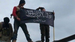 Al-Nusra Front activist wave their brigade flag atop a Syrian air force helicopter, at Taftanaz air base, captured by the rebels in Idlib province, northern Syria, January 2013 (photo credit: AP/Edlib News Network ENN, File)